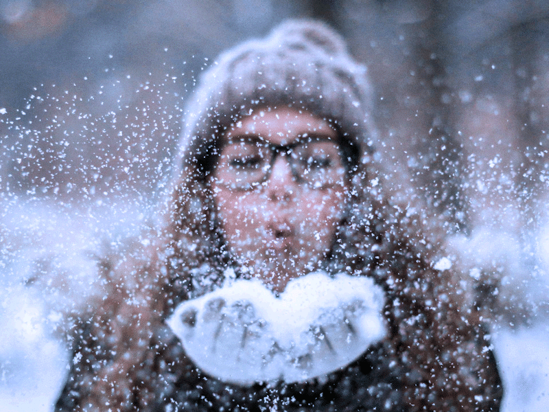 Woman in warm hat and coat blowing snow off her gloves. Don't suffer from SAD in winter - follow our tips to improve your mental health.